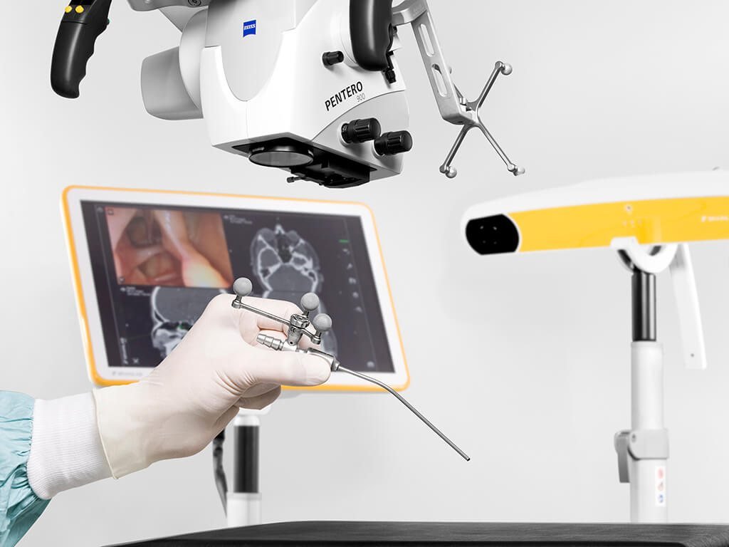 Hand holding a navigated instrument beside a microscope and navigation screen